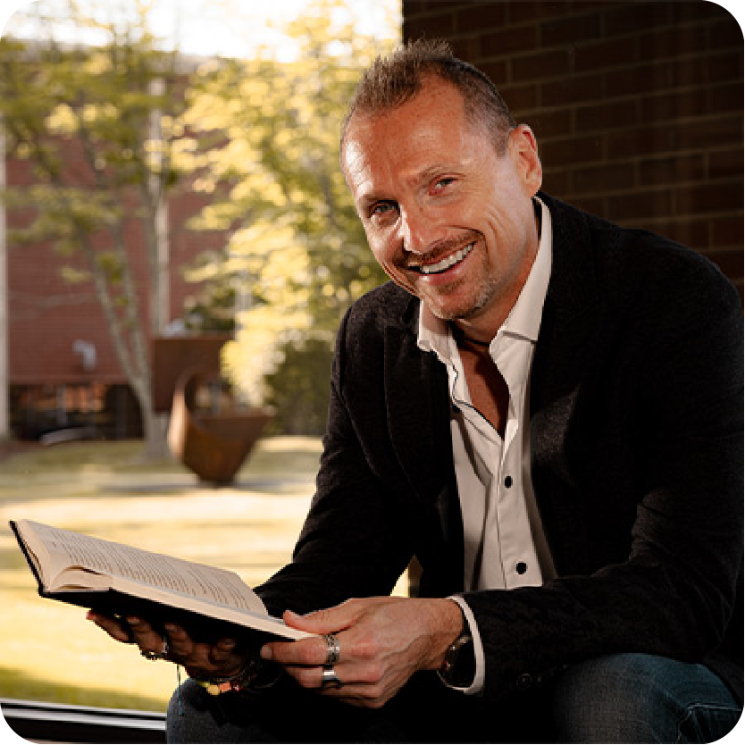 Joe Hudicka, co-founder of Evenflow, smiling while reading a book, representing leadership, innovation, and a passion for learning